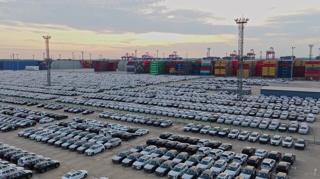Aerial view of automobile logistics yard and container stacks at seaport during sunset