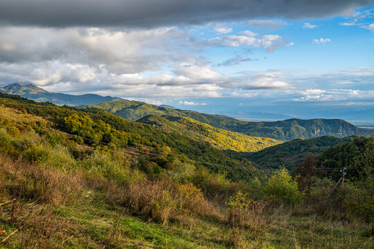 Mountains rise in South Ossetia with green hills and cloudy sky in view during late afternoon sun