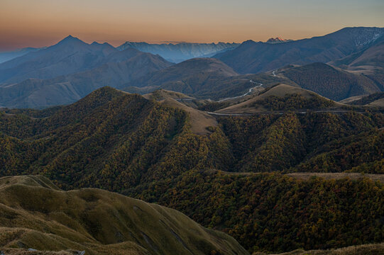 Mountains rise across the landscape in Chechnya, showcasing rugged terrain and diverse vegetation under fading light