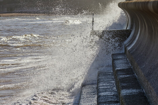 Waves crash against the sea wall on the coast of the English Channel in Teignmouth, Devon, during a sunny day