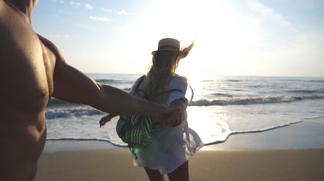 Beautiful girl holding male hand and running to the water at the sea beach. Follow me shot of happy woman pull her boyfriend to the coast. Young couple spending time together. Slow motion