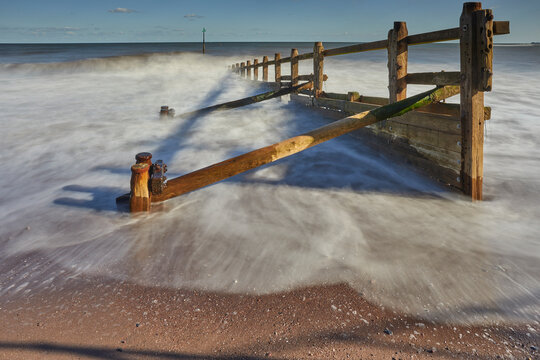 Waves crash against wooden groyne at beach in Teignmouth, capturing the essence of coastal life in Devon