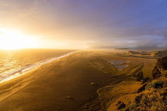 Golden sunset over Dyrholaey coastline with waves breaking on black sand beach