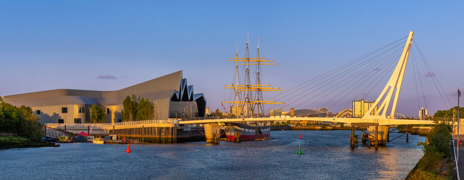 Scenic view showing a bridge and a tall ship moored near modern buildings at sunset in a waterfront location
