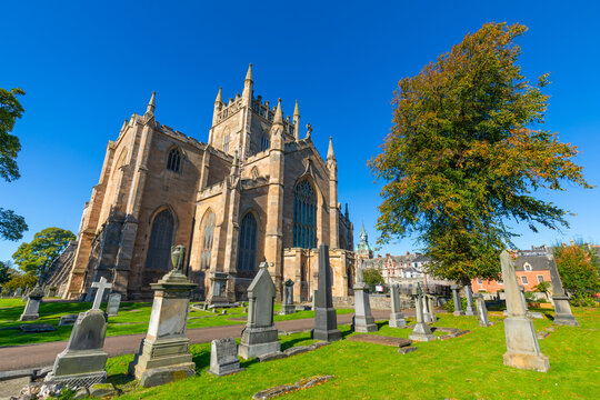 Dunfermline Abbey stands tall in the sunlight surrounded by gravestones and green grass in Dunfermline, UK