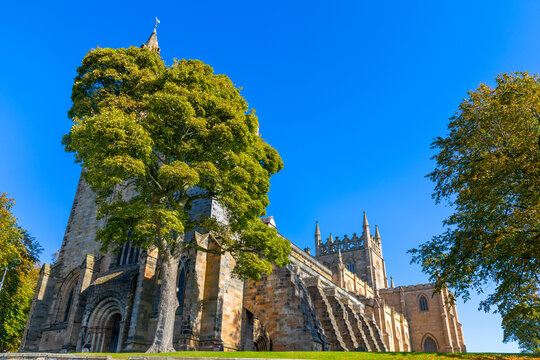 Dunfermline Abbey stands under a clear blue sky with trees surrounding its historic structure in Dunfermline, Fife, Scotland, United Kingdom