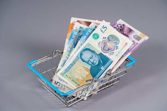 Pound sterling notes in a small shopping basket on a grey background