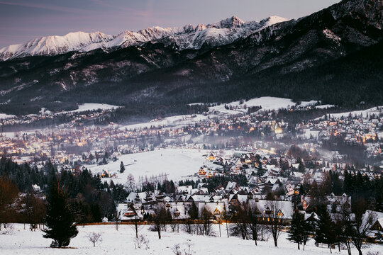 Winter night scene with snow-covered mountains and village lights in Zakopane, Poland, showcasing the beauty of the High Tatras