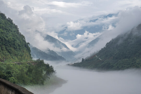 Misty mountain valley in Sichuan China with clouds covering slopes and a river flowing through the landscape
