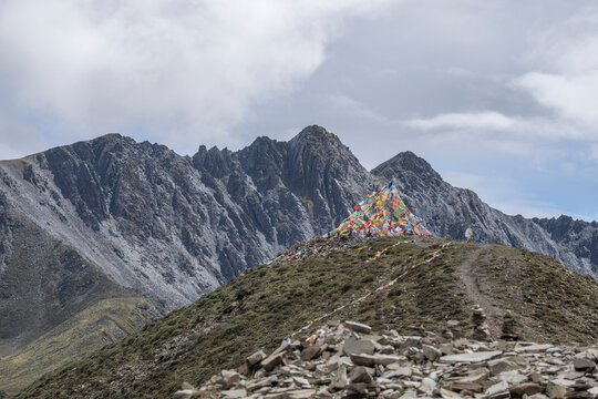 Dramatic clouds surround Zimei mountain pass with prayer flags and rugged peaks in Sichuan, China during a cloudy day