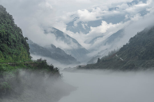 Mist flows between green slopes and a winding river in a mountain valley of western Sichuan, China