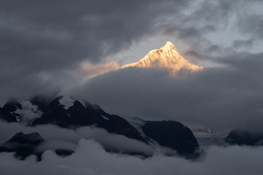 Golden light shines on Kawagebo Peak at dawn in Yunnan China with clouds surrounding the mountain