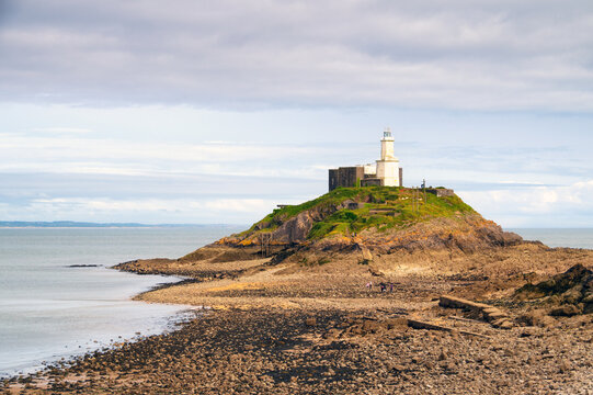 People walking towards the Lighthouse at Mumbles Head during low tide in Swansea, Wales
