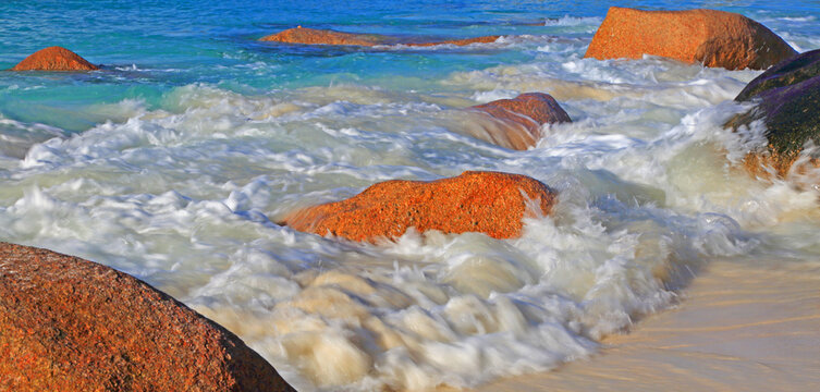 Waves crash against rocks at Anse Lazio beach in Seychelles during bright daylight hours
