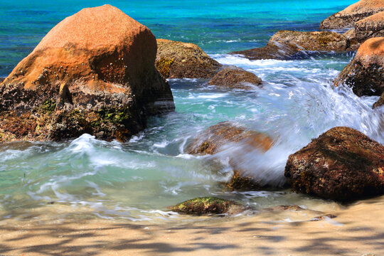 Waves crash over rocks at Anse Lazio beach in Seychelles during a sunny day with turquoise water and soft sand nearby