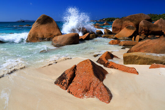 Waves crash on rocks at a beautiful beach with clear water and bright sunlight in Seychelles