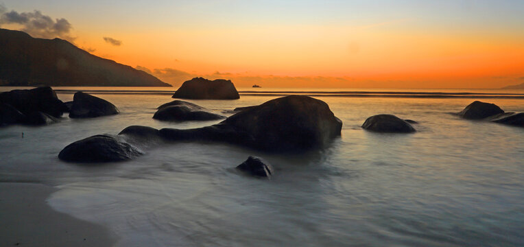 Sunset over the water with rocks at Beau Vallon beach, on Mahe in Seychelles during evening hours
