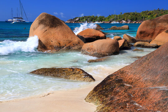 Waves crash against rocky shore at Anse Georgette on Praslin island with boats in the background