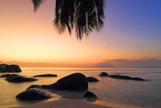 Colorful sunset at Beau Vallon Beach with rocks and palm trees near the water in Seychelles
