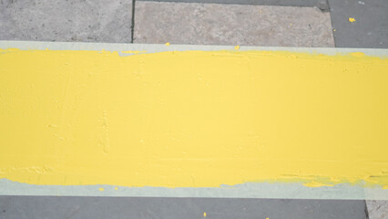 Fototapeta premium fresh thick yellow paint strip applied to a gray stone sidewalk