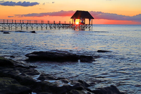 Sunset illuminates the pier at Pointe aux Piments in Mauritius with ocean waves lapping shore