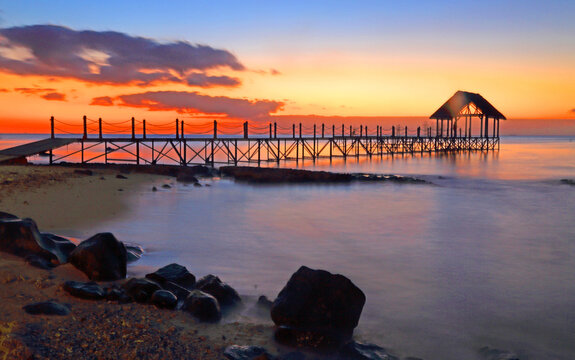 Sunset view over a pier with water reflections and clouds in Pointe aux Piments, Mauritius