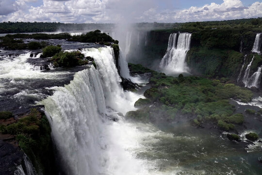 Water flows from Iguazu Falls in Brazil with clouds and greenery in view during the day