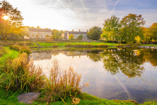 Reflections in a village pond at Monyash during autumn with buildings and trees in view