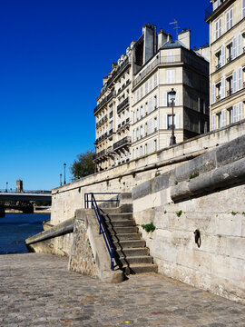 Buildings and steps along the banks of Ile St Louis in Paris with clear blue sky