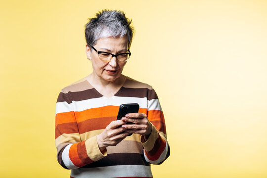 Senior woman wearing glasses and striped sweater, actively engaging with her smartphone. She is focused on the device