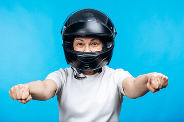 Woman in a black full-face motorcycle helmet and white t-shirt, excitedly holding fists forward on blue background © Petro
