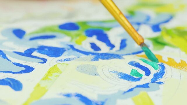 Close-up cinematic footage of brush applying green paint to detailed art canvas, showing creative process and artistic expression.