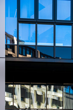 Blue glass windows hold layered reflection on an abstract architecture facade where building grid and exterior detail create a precise urban pattern
