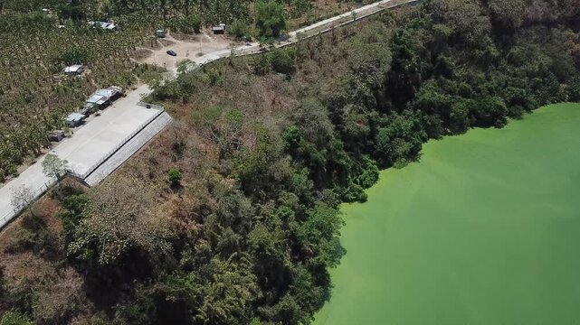 Rural road paved alongside a secluded lake surrounded by dense forests of Lake Tikub, Tiaong, Quezon, Philippines. Drone aerial shot