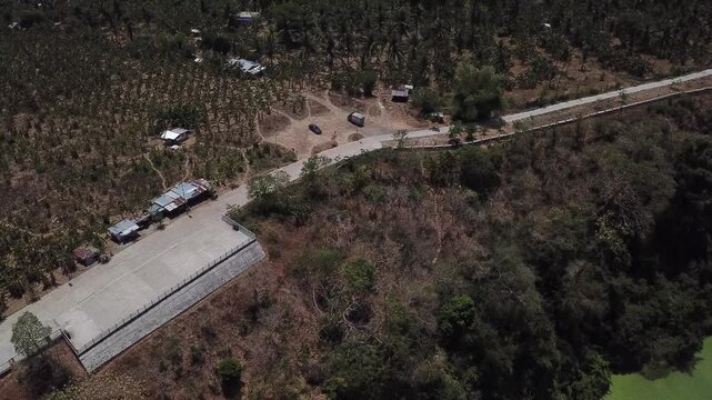 Rural road paved alongside a secluded lake surrounded by dense forests of Lake Tikub, Tiaong, Quezon, Philippines. Drone aerial shot