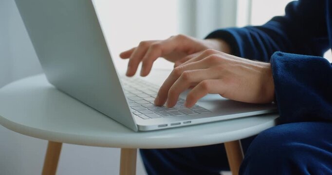 Man in blue comfortable clothes typing on modern laptop at home.