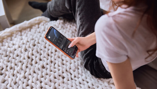 Woman checking banking app balance on smartphone while sitting on cozy bed. Concept of personal budgeting, mobile finance, account management, savings and secure digital banking.