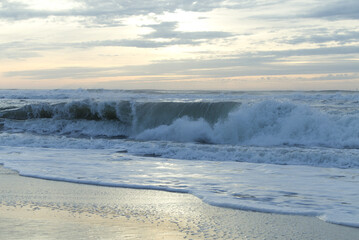 Ocean waves crashing on a sandy beach at sunrise with soft clouds in the sky © milenofrigatto
