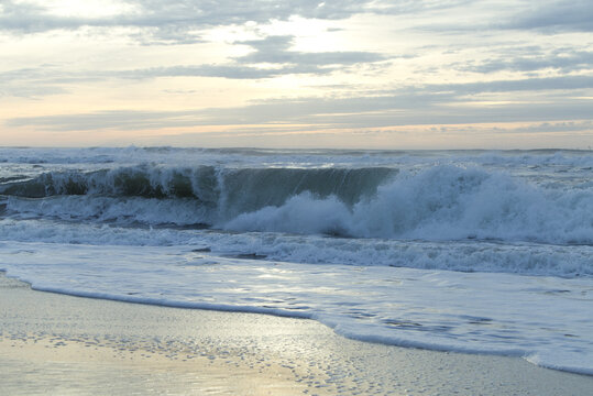 Ocean waves crashing on a sandy beach at sunrise with soft clouds in the sky
