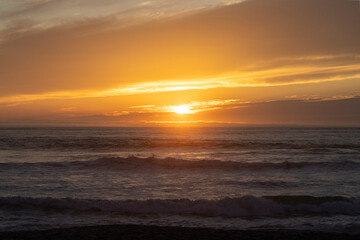 Obraz premium Golden sunset over the ocean with gentle waves and dramatic clouds