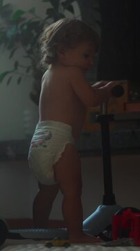 Toddler riding scooter indoors while wearing diaper during playful home activity capturing balance learning, mobility and authentic early childhood development