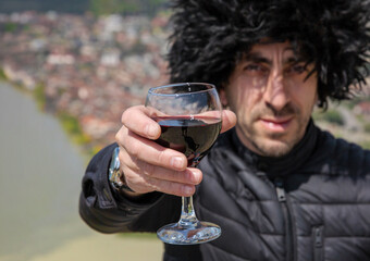 Obraz premium Georgian man in a papakhi with a glass of wine. Selective focus.
