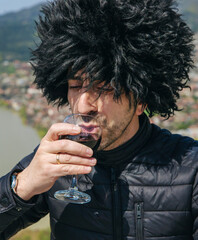 Obraz premium Georgian man in a papakhi with a glass of wine. Selective focus.