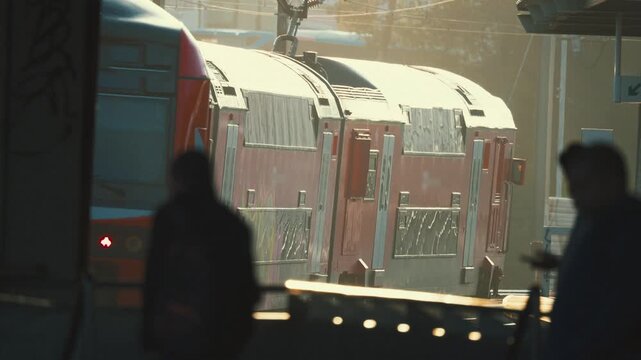 Train arrives at the station as people move around and interact with their devices in the early morning light