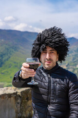 Obraz premium Georgian man in a papakhi with a glass of wine. Selective focus.