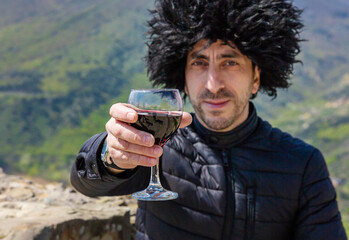 Obraz premium Georgian man in a papakhi with a glass of wine. Selective focus.
