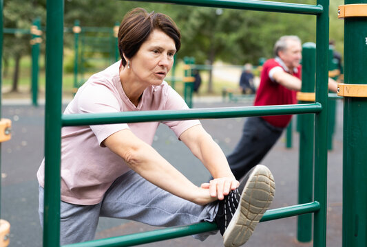 elderly woman stretches on the bars in an outdoor sports area