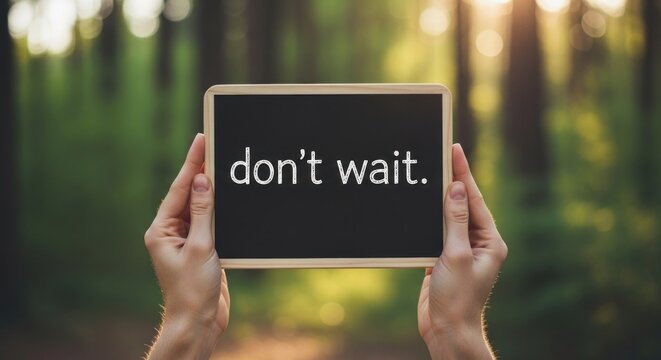 Person holding a chalkboard with the message dont wait in a forest setting.