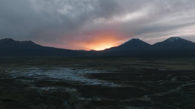 Aerial sunset over Sajama plains in Bolivia, warm golden light illuminating vast Altiplano landscape. Minimalist scenery with long shadows and dramatic sky.
