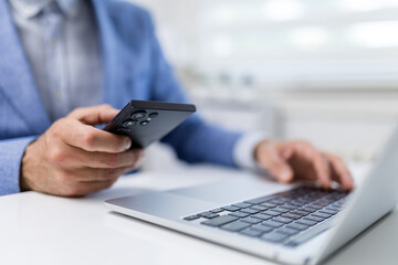 Fototapeta premium Businessman Using Smartphone Beside Laptop in Office